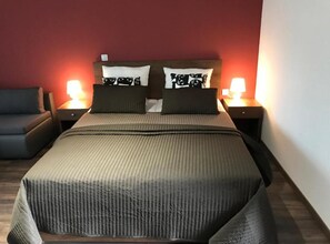 Ein Bett mit Kopfteil, zwei Nachttische mit Lampen, ein graues Sofa und eine rote Wand.