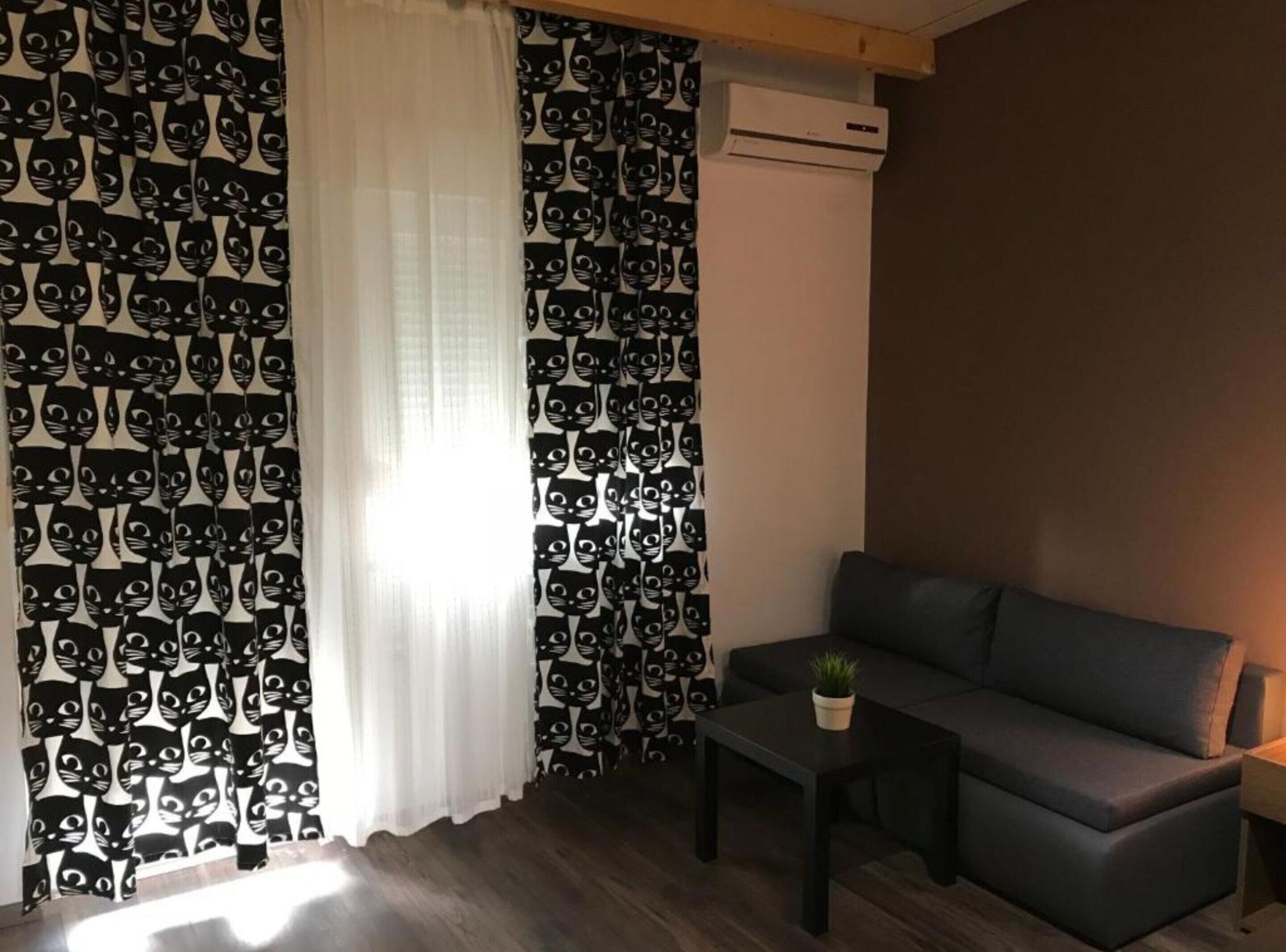 Una sala de estar con un sofá, una mesita con una planta y una ventana con cortinas.