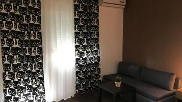 Una sala de estar con un sofá, una mesita con una planta y una ventana con cortinas.