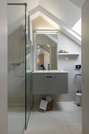 Ein modernes Badezimmer mit Glasdusche, weißem Waschtisch und Dachfenster.