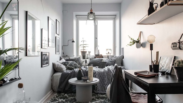 A cozy room with a bed, a round table, and a desk with a chair. There are framed pictures on the wall, a potted plant, and a window with a view. - Houyam Location (Flemalle)