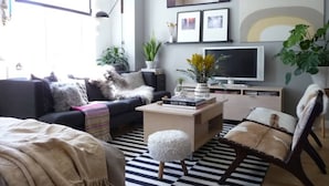 A modern living room with a sofa, coffee table, and armchair, a flat-screen TV, and decorative plants. - Houyam Location (Flemalle)