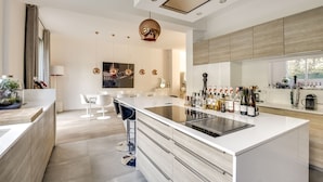 A modern kitchen with a central island, bar stools, and a large window. - Houyam Location (Flemalle)