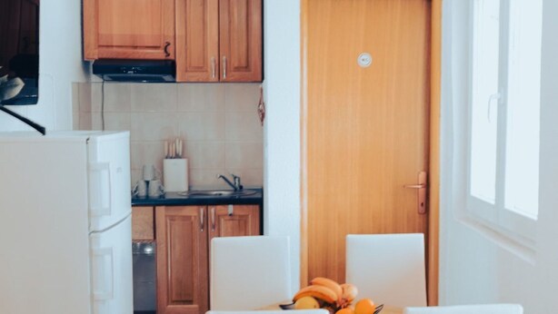 Eine kleine Küche mit Holzschränken, einem weißen Kühlschrank und einem Esstisch mit vier Stühlen.