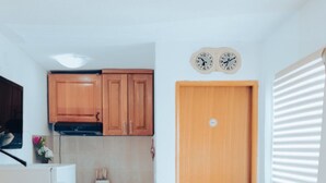 Eine kompakte Küche mit Holzschränken, einem weißen Kühlschrank und einem Esstisch mit Stühlen. Auf dem Tisch steht eine Obstschale.