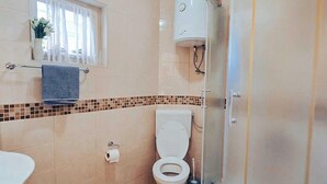 Ein Badezimmer mit Toilette, Waschbecken, Dusche und einem Fenster mit Vorhängen.