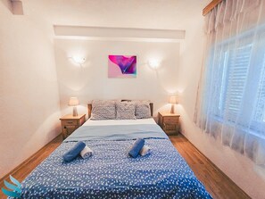 Ein Schlafzimmer mit einem Bett, zwei Nachttischen, einem Wandbild und einem Fenster mit Vorhängen.
