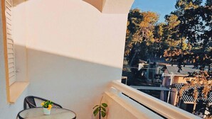 Ein Balkon mit einem kleinen Tisch, Stühlen, einem Blumentopf und Blick auf Bäume und Gebäude.