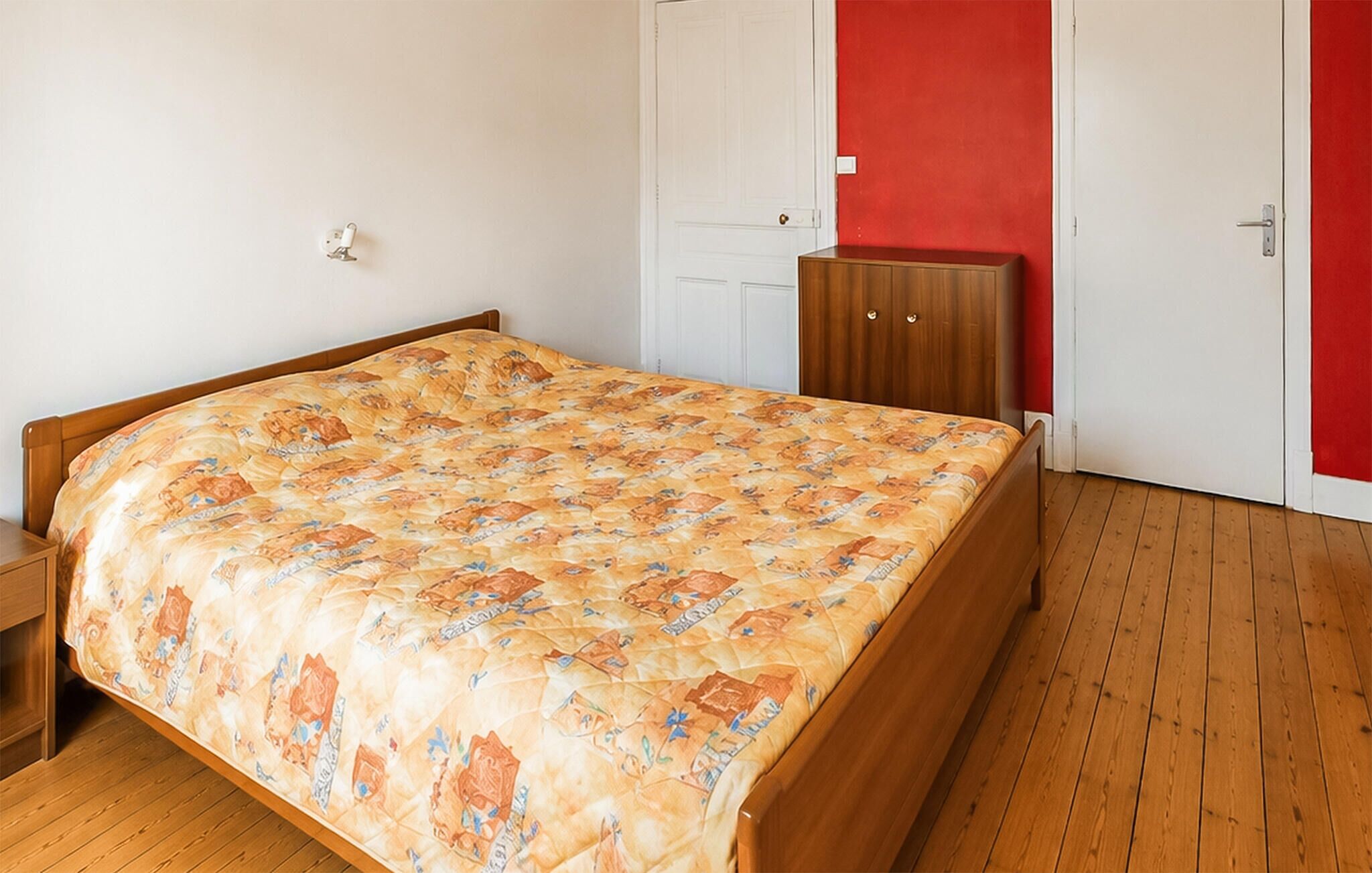 A bedroom with a wooden bed, a red wall, and a white door.
