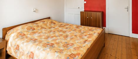 A bedroom with a wooden bed, a red wall, and a white door.