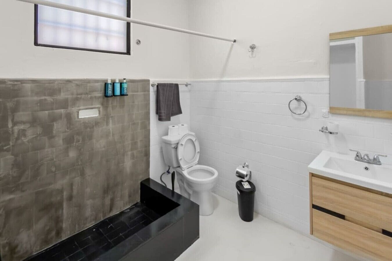 A modern bathroom with a black sink, white tiles, a toilet, and a mirror.