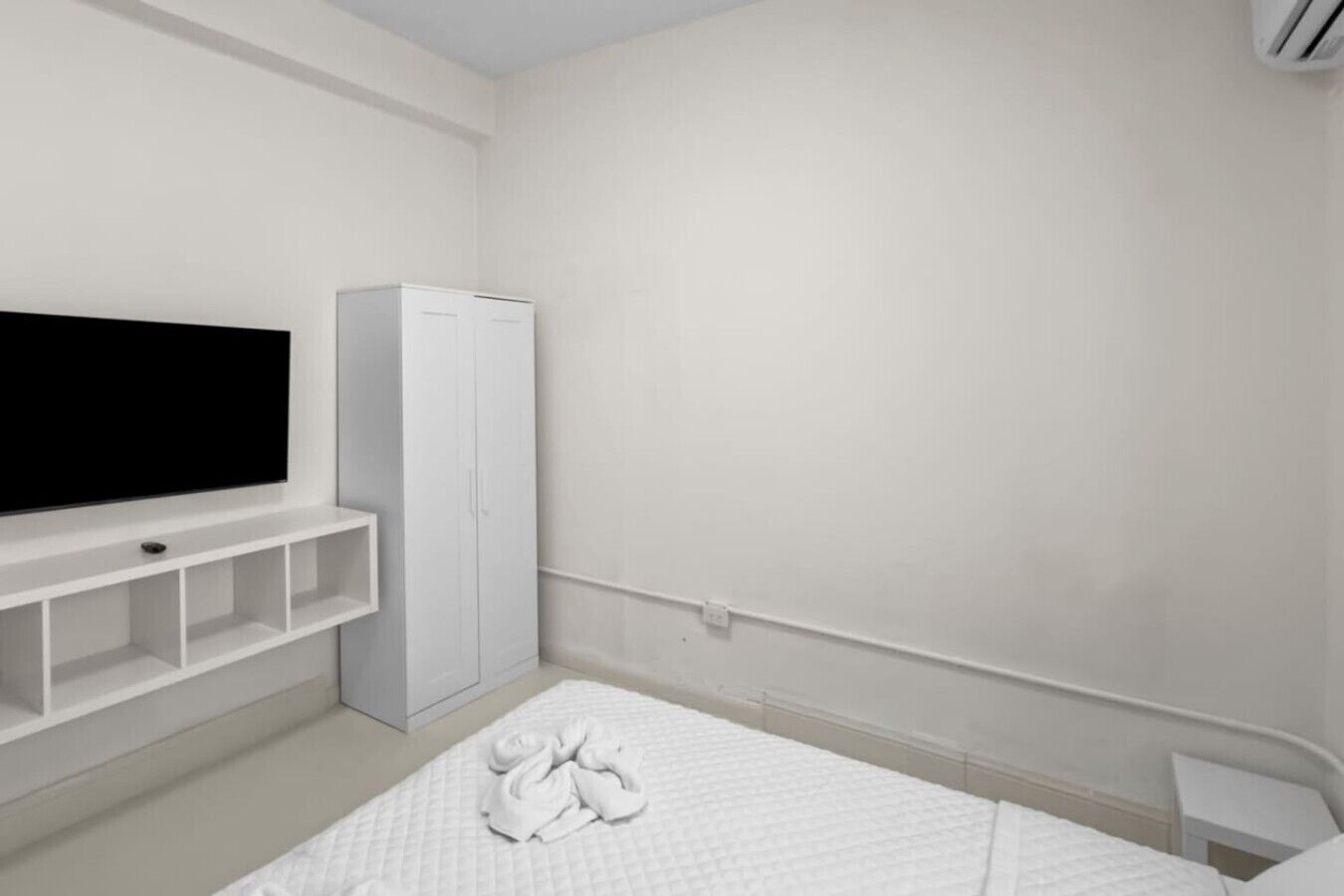 A minimalist bedroom with a flat-screen TV, a wardrobe, and a neatly made bed.
