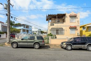 A street with two parked SUVs, a multi-story building with a balcony, and a white fence. - Casa Magnolia Apt 6 | Santurce Multifamily House (San Juan de Puerto Rico)