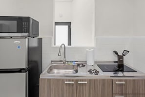 A compact kitchen with a built-in microwave, stainless steel sink, and a modern induction cooktop. - Casa Magnolia Apt 6 | Santurce Multifamily House (San Juan de Puerto Rico)