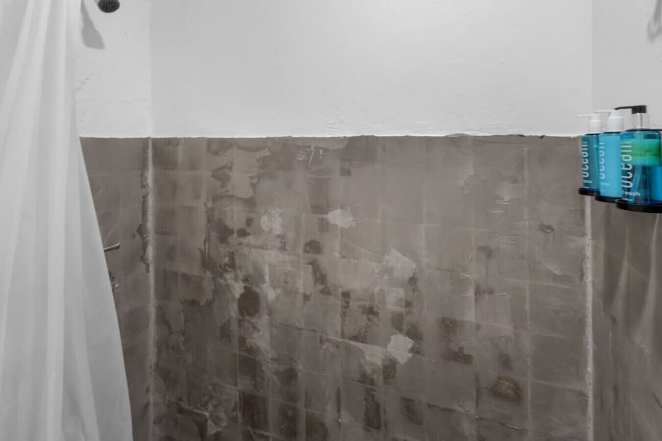 Een badkamer met douchegordijn, een handdoekhouder met flesjes en een betegelde muur.