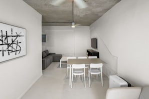 A modern interior with a dining table, chairs, a sofa, and a mounted TV. - Casa Magnolia Apt 8 | Santurce Multifamily House (San Juan de Puerto Rico)