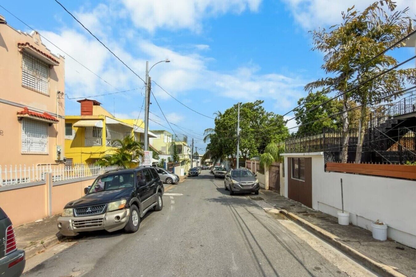 Une rue résidentielle bordée de voitures garées, de maisons et d’un ciel dégagé.