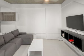 A modern living room with a grey sectional sofa, a white coffee table, a flat-screen TV on a black stand, and a white door. - Casa Magnolia Apt 8 | Santurce Multifamily House (San Juan de Puerto Rico)