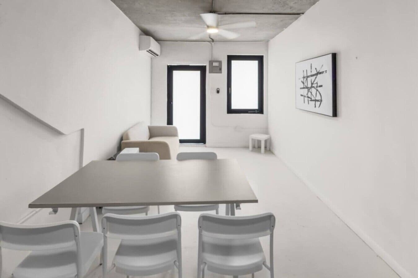 Una sala de conferències amb una taula gran, cadires blanques, un sofà i un ventilador de sostre.