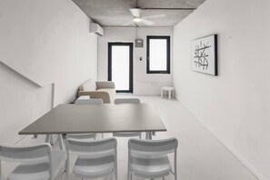 A conference room with a large table, white chairs, a sofa, and a ceiling fan. - Casa Magnolia Apt 8 | Santurce Multifamily House (San Juan de Puerto Rico)