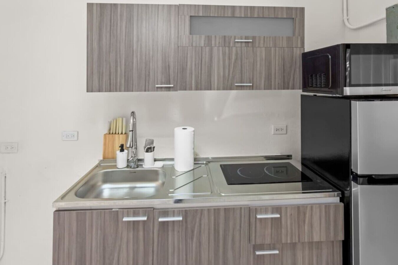 Una cocina compacta con un lavamanos de acero inoxidable, un microondas y un horno empotrado.