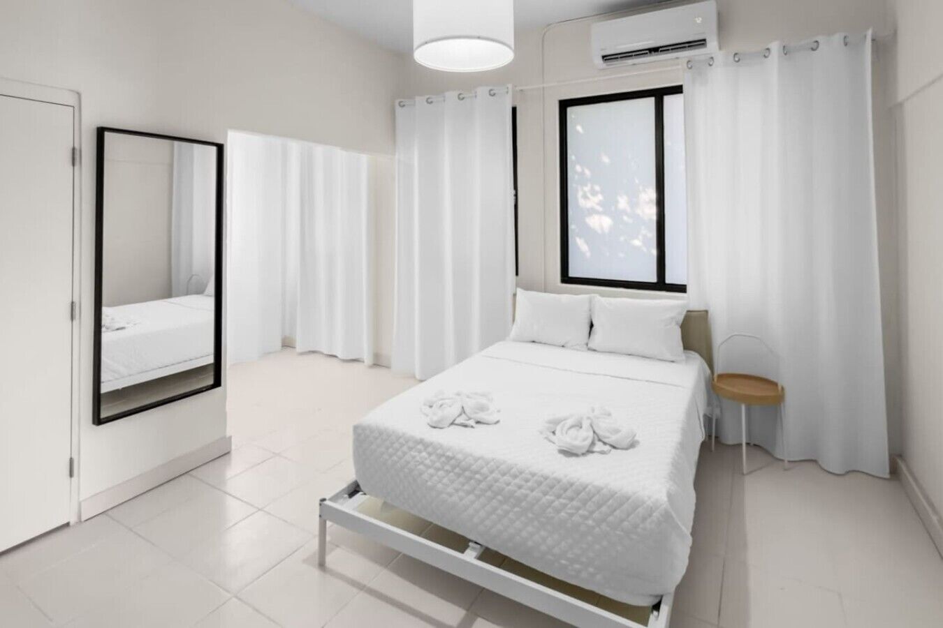 A modern bedroom with a bed, a bedside table, a chair, a window, and a mirror.