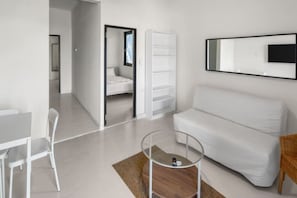 Ein modernes, minimalistisches Zimmer mit einem weißen Sofa, einem kleinen runden Couchtisch, einem weißen Wand-Fernseher und einem weißen Kleiderschrank.