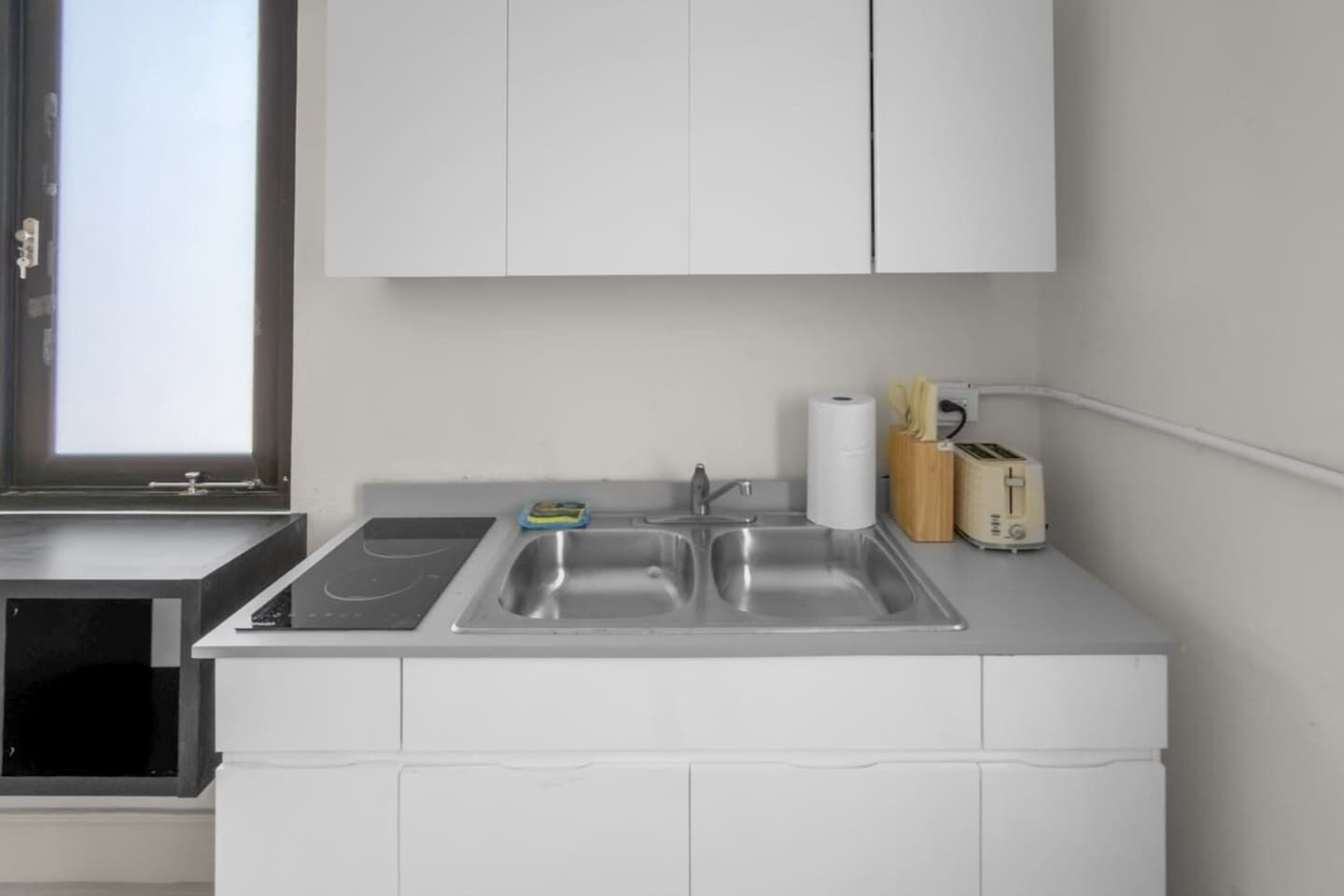 Une cuisine moderne dotée d’une cuisinière intégrée, d’un évier à deux bacs et d’une fenêtre laissant entrer la lumière naturelle.
