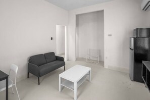 A minimalist living room with a sofa, a coffee table, a chair, and a refrigerator. - Casa Magnolia Apt 7 | Santurce Multifamily House (San Juan de Puerto Rico)