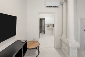 A modern room with a flat-screen TV, a small round table, and a doorway leading to a bathroom. - Casa Magnolia Apt 2 | Santurce Multifamily House (San Juan de Puerto Rico)