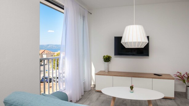A modern living room with a sofa, a round coffee table, a TV mounted on the wall, and a balcony with a view of the sea. - Apartments Dva Galeba - Premium One Bedroom Apartment With Sea View (Bol)