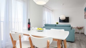 A modern living room with a dining area, featuring a sofa, a TV mounted on the wall, and a table with chairs. - Apartments Dva Galeba - Premium One Bedroom Apartment With Sea View (Bol)