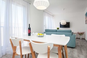 A modern living room with a dining area, featuring a sofa, a TV mounted on the wall, and a table with chairs. - Apartments Dva Galeba - Premium One Bedroom Apartment With Sea View (Bol)