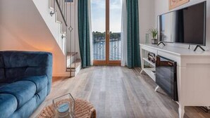 A modern living room with a blue sofa, a flat-screen TV, and a balcony with a view. - Luxury Room With Sea View (Trogir)