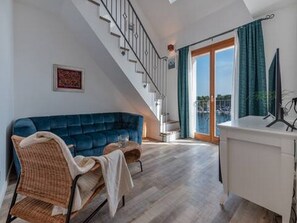 Ein Wohnzimmer mit einem blauen Sofa, einem Korbstuhl, einem weißen Schrank und einer Treppe, die zu einem Balkon führt.
