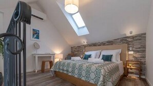 A bedroom with a sloped ceiling, a bed with patterned bedding, a desk, and a wall-mounted lamp. - Luxury Room With Sea View (Trogir)