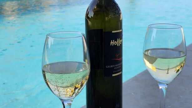 A bottle of wine and two glasses on a poolside table with a pool and lounge chairs in the background. - Villa Marija - Two Bedroom Apartment With Sea View (Novalja)