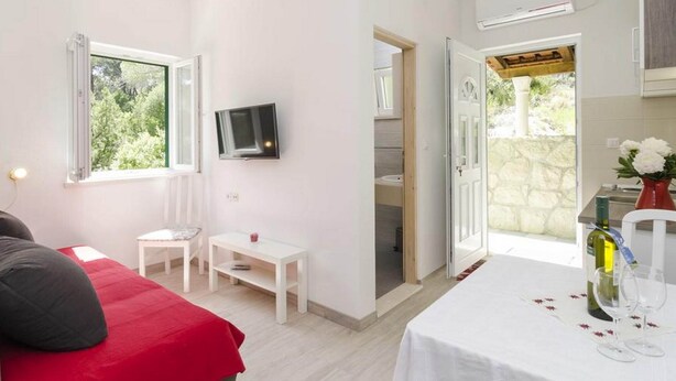 A hotel room with a bed, a TV, a small table, and a dining area with a bottle and glasses. - Apartments Matusko Mljet - One Bedroom Apartment With Balcony and Sea View (Mljet)
