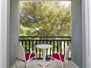 Ein Balkon mit zwei weißen Stühlen und einem kleinen runden Tisch, mit Blick auf einen Baum.
