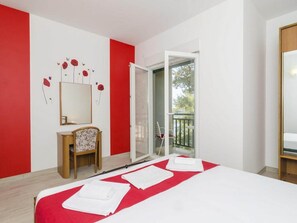 Ein Hotelzimmer mit Bett, Stuhl, Schreibtisch, Spiegel und einem Balkon.