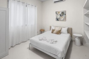 A hotel room with a bed, a chair, a small table, and a painting on the wall. - Casa Magnolia Apt 1 | Santurce Multi Family House (San Juan de Puerto Rico)