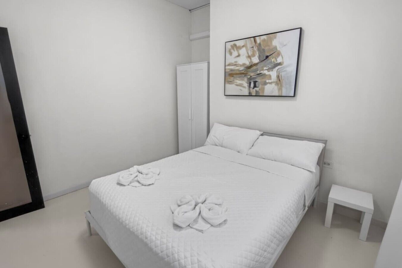 Ein Schlafzimmer mit einem Bett, Kissen, einem Nachttisch, einem Kleiderschrank und einem Bild an der Wand.