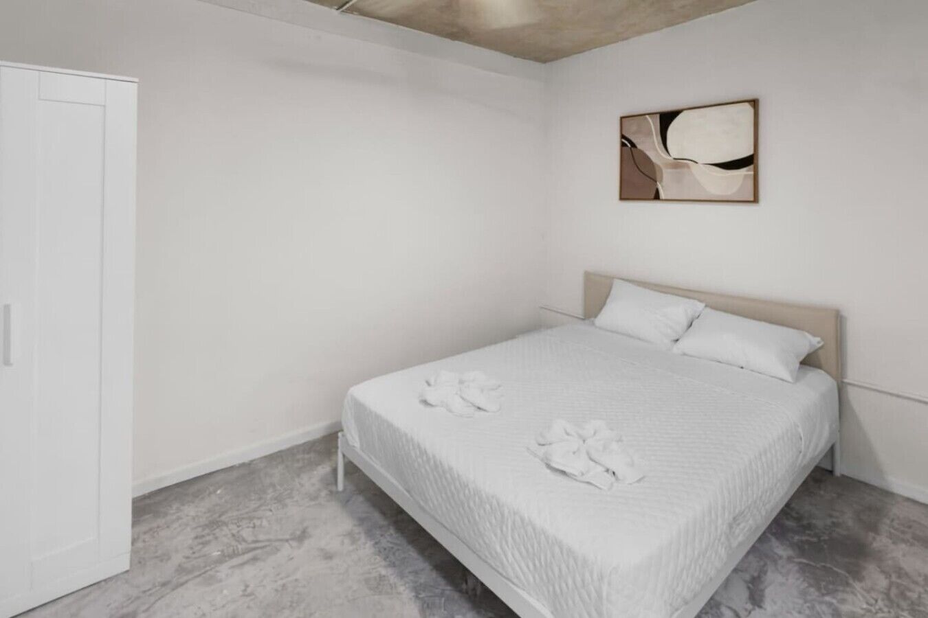 A bedroom with a bed, white walls, a door, and a painting.