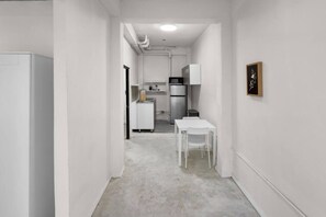 A narrow hallway leading to a kitchenette with a refrigerator, microwave, and sink. A white table and chair are positioned in the hallway. - Casa Magnolia Apt 9 | Santurce Multifamily House (San juan de Puerto Rico)