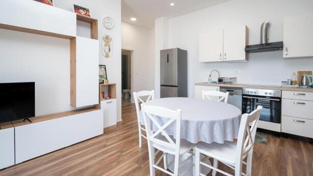 Una cocina moderna con armarios blancos, horno empotrado y una zona de comedor con mesa y sillas redondas.
