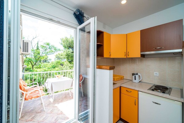 Eine moderne Küche mit orangefarbenen Schränken, einer weißen Arbeitsplatte und Blick auf einen Balkon mit Gartenmöbeln.