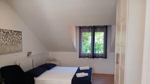 A bedroom with a bed, a chair, a small table with a plant, a window with curtains, and a radiator. - Apartment & Rooms Papa - Studio Apartment With Balcony and Partial Sea View (Zupa dubrovacka)
