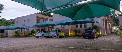 A paved driveway leading to a building with multiple green umbrellas providing shade.