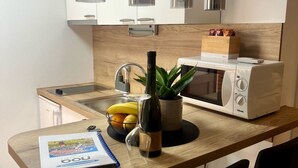 A modern kitchen with a wooden countertop, a microwave, a bottle of wine, and a plant. - Apartments Noa Old Town - Studio - Ground Floor (Dubrovnik)