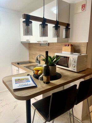 A modern kitchen with a wooden countertop, a microwave, a bottle of wine, and a plant. - Apartments Noa Old Town - Studio - Ground Floor (Dubrovnik)
